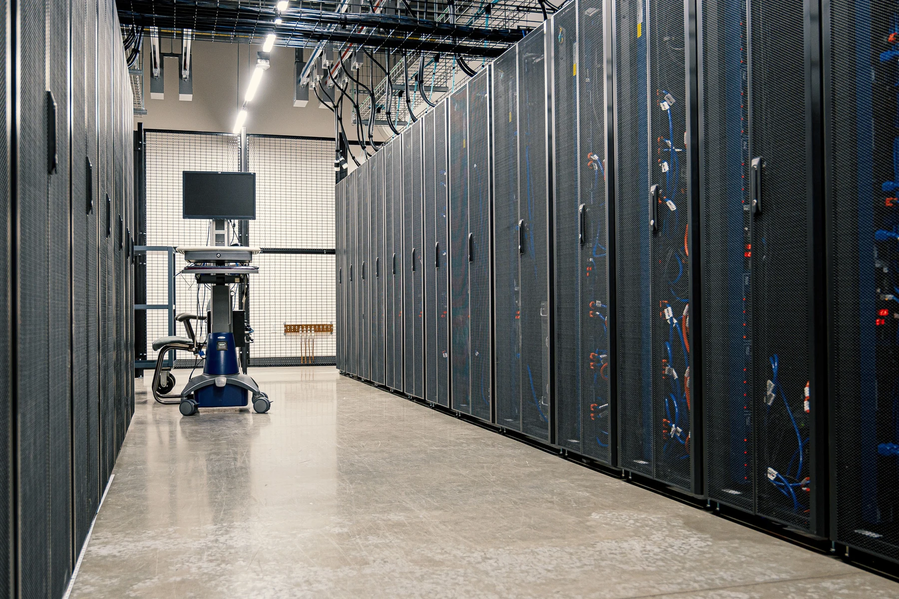 Rows of dark server cabinets and overhead cable trays along a data-centre aisle